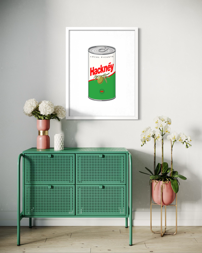 A framed pop-art print of a green and silver Hacknéy can hangs on a light gray wall above a mint green cabinet, styled with white flowers in pink and white ceramic vases.
