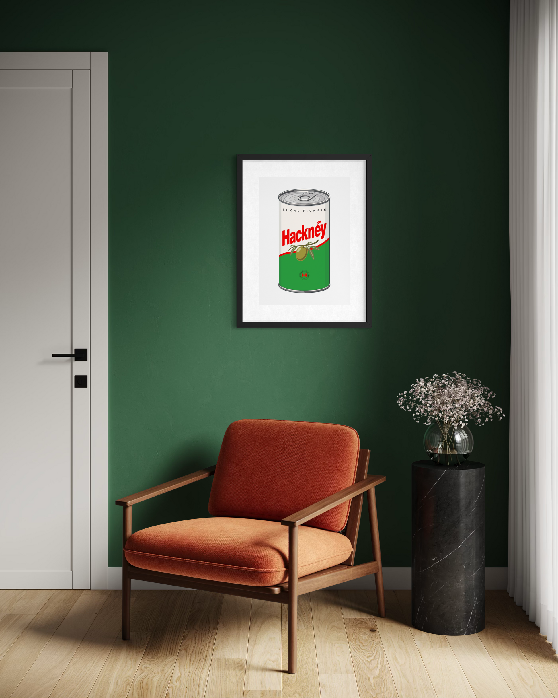 A framed art print of a vintage Hackney olive can poster hangs on a dark green wall in a modern room setting with an orange armchair and a black marble side table.